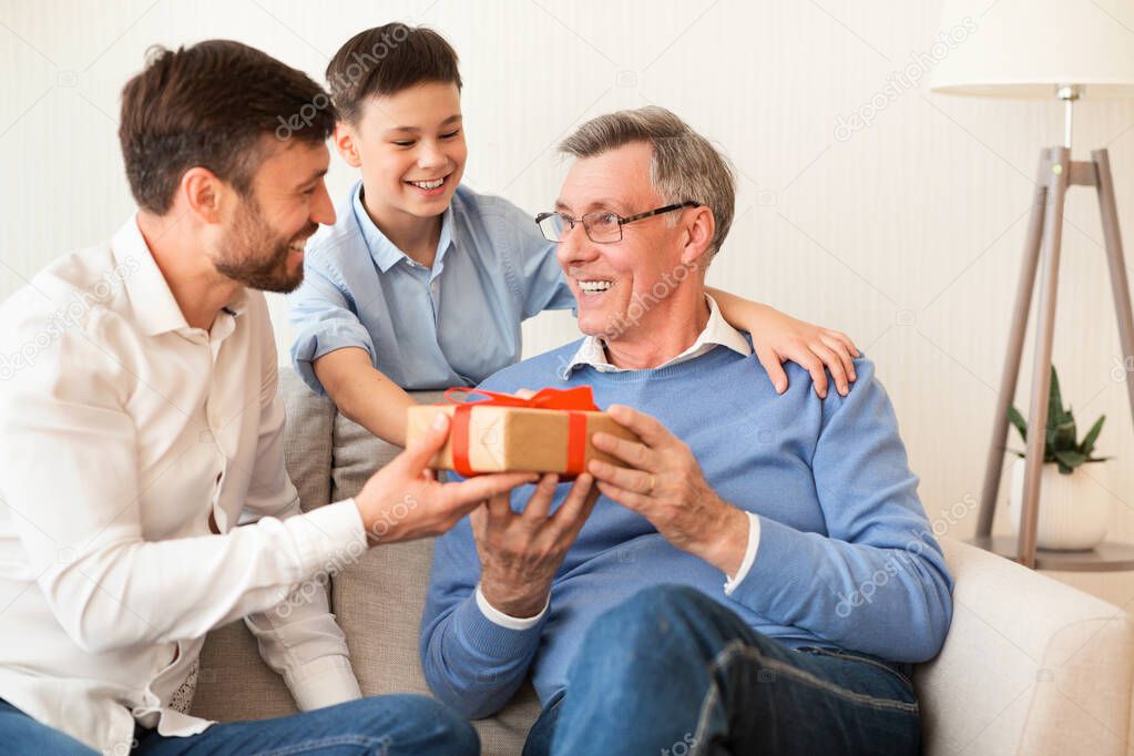 Father And Son Congratulating Grandpa Giving Birthday Gift At Home