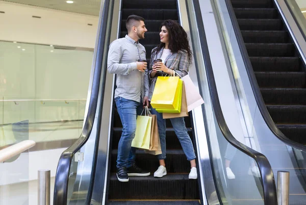 Счастливая пара пьет кофе, спускаясь по эскалатору. Лицензионные Стоковые Изображения
