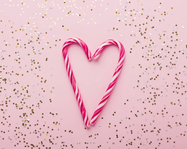 Candy canes in shape of heart on pink background