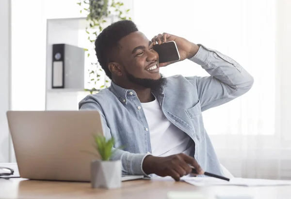 Smiling african american employee talking on mobile phone at workplace — Stock Fotó