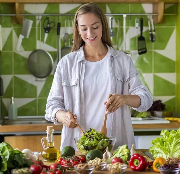 Jonge lachende vrouw die thuis groentesalade maakt — Stockfoto