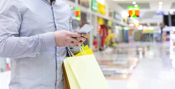 Man searching new clothes on cellphone, walking in shopping mall — Stock Photo, Image