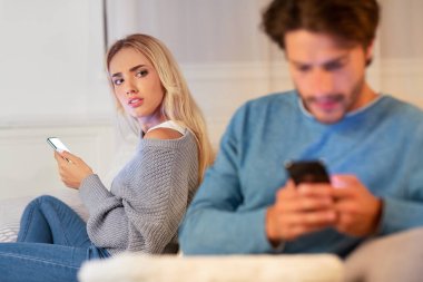 Kadın, kocanın cep telefonuyla konuşmasını izliyor. İçeride koltukta oturuyor.