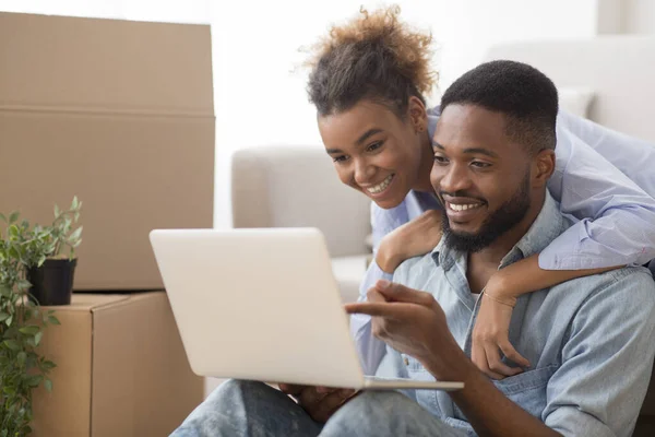 Чорні подружжя за допомогою ноутбука сидячи на дивані в новому будинку — стокове фото
