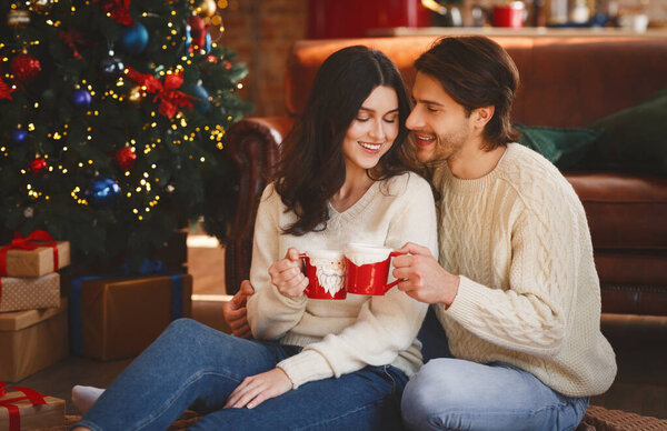 Couple in love having xmas cocoa next to Christmas tree