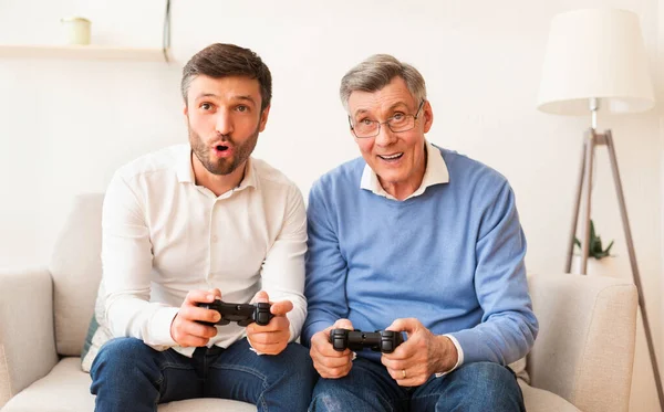 Hijo y anciano padre jugando videojuego sentado en sofá interior — Foto de Stock
