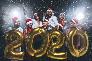 Mutlu arkadaşlar 2020 yılını karşılıyor, ellerinde altın balonlar var.