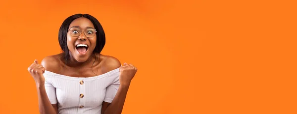 Gelukkig zwart vrouw schreeuwen schudden vuisten staande, oranje achtergrond, panorama — Stockfoto
