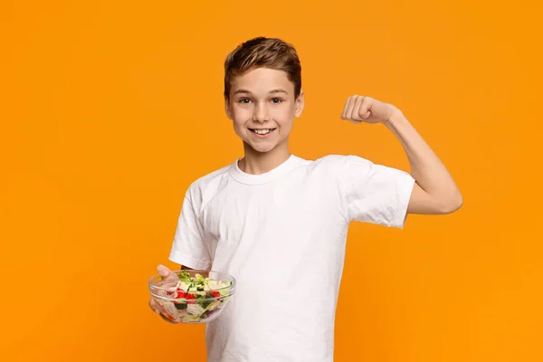 Tonårspojke med färsk grönsakssallad demonstrerar sina biceps — Stockfoto