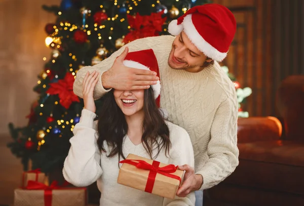 산타 모자를 쓰고 아내에게 선물을 하는 잘생긴 남자 — 스톡 사진