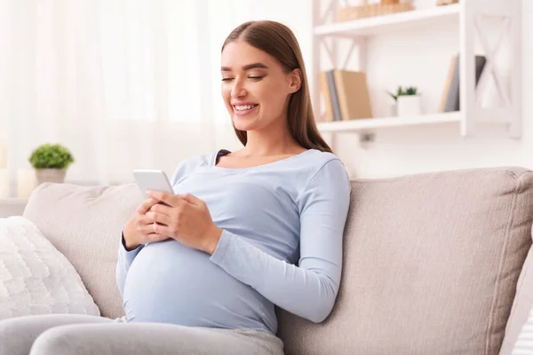 Pregnant Woman Texting On Cellphone Sitting On Sofa At Home — Stok Foto