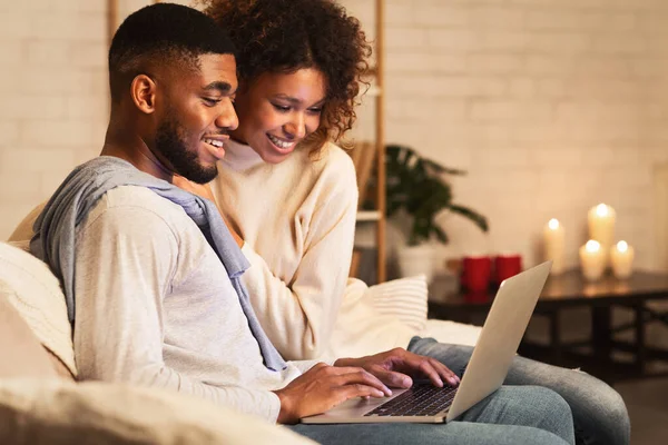 Emocionada pareja afro navegar por la red en el ordenador portátil disfrutando de una noche acogedora — Foto de Stock