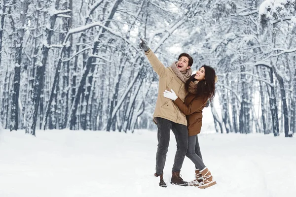 Fröhlicher Mann zeigt seiner Freundin etwas, das im verschneiten Park steht — Stockfoto