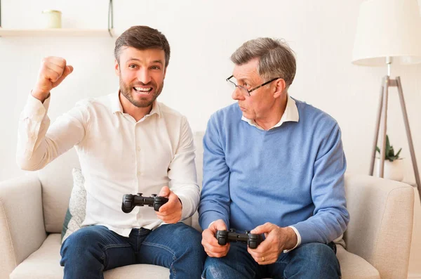 Hombre mayor perdiendo el videojuego a hijo maduro en casa — Foto de Stock