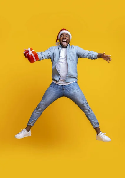 Chico afro muy alegre en santa hat saltando con caja de regalo — Foto de Stock