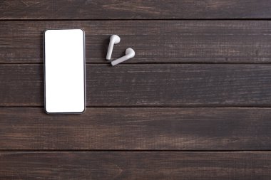 Boş ekranlı akıllı telefon ve tahta arka planda kablosuz kulaklık.