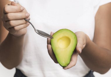 Beyaz arka planda duran kaşıkla Avokado yiyen kadın.