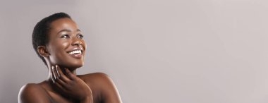 Mutlu afro kadın mükemmel tenine dokunuyor ve yan bakıyor.