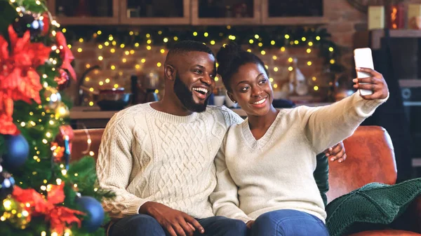 Neşeli afro çift evde Noel ağacının yanında selfie çekiyor.