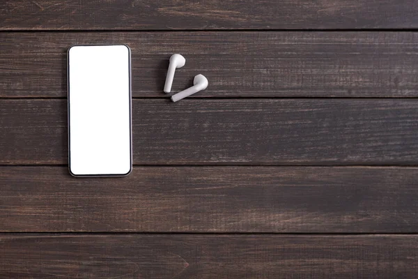 Smartphone con pantalla en blanco y auriculares inalámbricos sobre fondo de madera —  Fotos de Stock