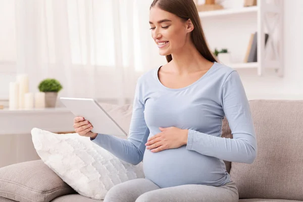 Gadis hamil Menggunakan Tablet Digital Duduk di Sofa Di Rumah — Stok Foto