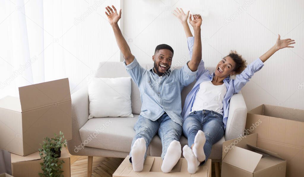 Happy Afro Couple Raising Hands Sitting On Sofa Indoor
