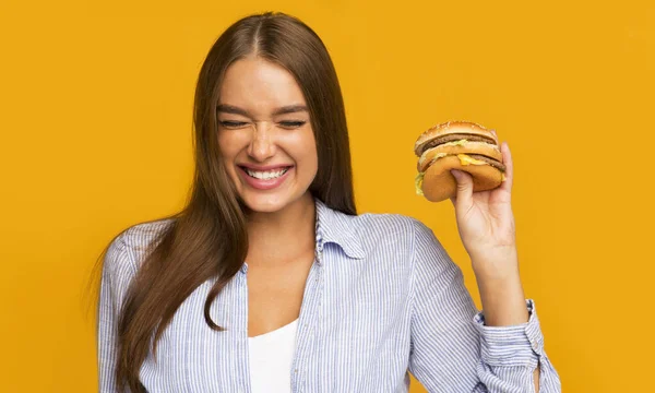 Millennial Girl Jedzenie hamburgera i śmiech stojąc w studio — Zdjęcie stockowe