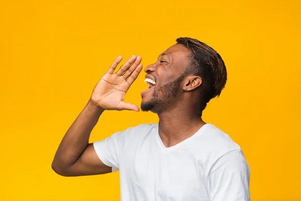 Afro Guy skriker håller handen nära munnen stående, gul bakgrund — Stockfoto