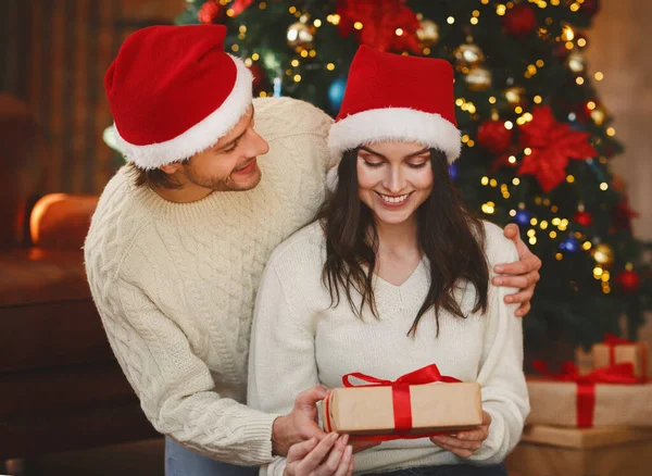 산타 모자를 쓴 쾌활 한 남자가 크리스마스 선물로 여자에게 인사한다 — 스톡 사진