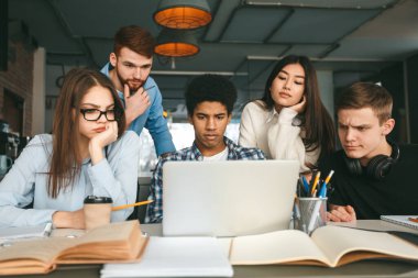 Akıllı ciddi öğrenciler dizüstü bilgisayarın önünde proje üzerinde çalışıyorlar.