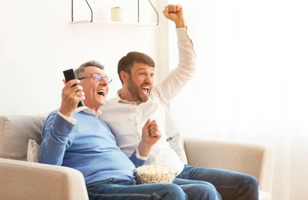 Älterer Vater und älterer Sohn sehen sich Spiel an und feiern Sieg in der Halle — Stockfoto