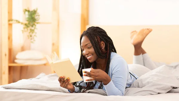 Chica afroamericana leyendo libro acostado en la cama en casa —  Fotos de Stock