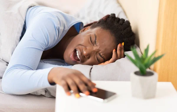 Афро-женщина касается головы, страдая от головной боли, лежащей в постели — стоковое фото