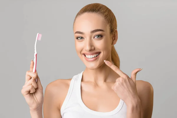 Kvinna med tandborste pekar på hennes perfekta tänder — Stockfoto