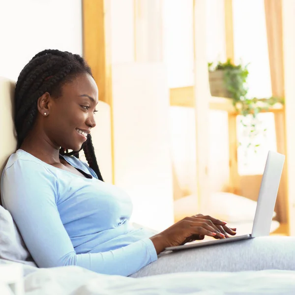 Happy Afro dame met behulp van laptop werkend zitten in de slaapkamer — Stockfoto