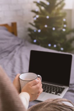 Beyaz bardaklı bir kadın ve siyah beyaz ekranlı yeni bir laptop.