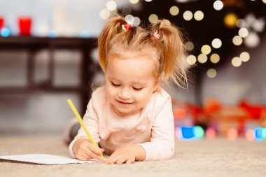 Küçük kız Xmas ağacının yanında çizim yapıyor.
