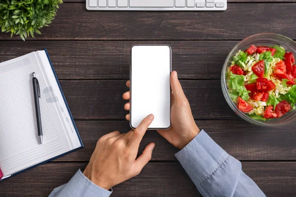 Akıllı telefonu boş ekranda kullanan ve sebze salatası yiyen bir adam.
