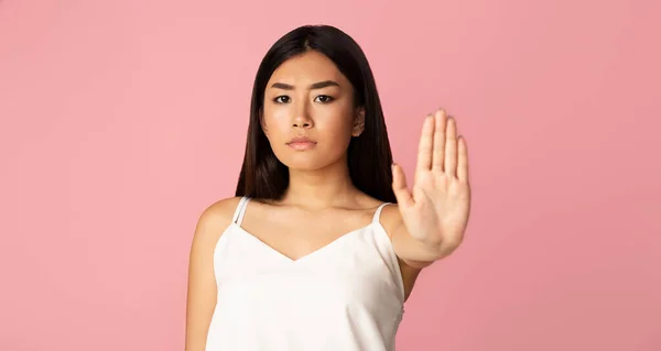 Serious asian girl showing stop gesture, pink background — ストック写真