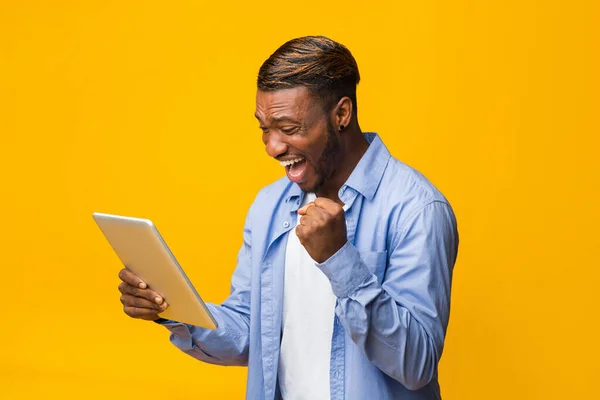 Opgewonden zwarte man die de tablet vasthoudt die Ja staat, gele achtergrond — Stockfoto