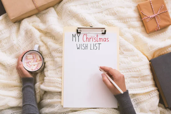 Woman writing with pen on clipboard and drinking hot cocoa — Stock Photo, Image