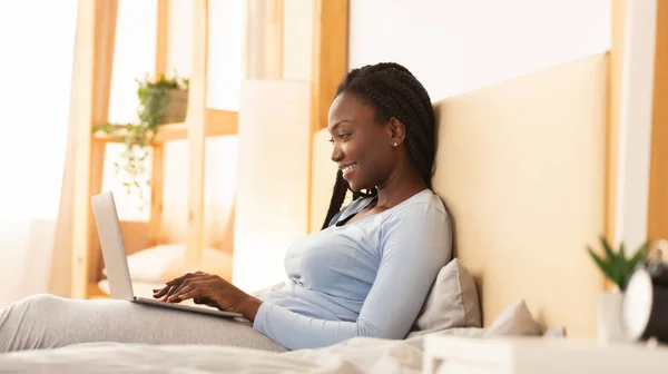 Афроамериканка работает на ноутбуке сидя в постели, Панорама — стоковое фото