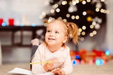 Sevimli küçük çocuk Noel ağacının yanında yerde yatıyor.