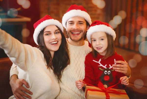Üç kişilik neşeli bir aile Noel arifesinde selfie çekiyor.