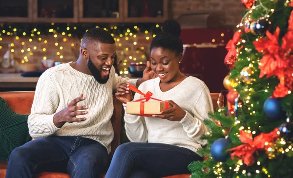 Χαρούμενη έκπληκτη μαύρη γυναίκα ξετυλίγει Χριστουγεννιάτικο δώρο από το αγόρι της — Φωτογραφία Αρχείου