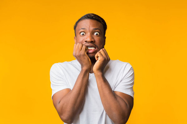 Испуганный афро-парень, трогающий лицо, позирующий на жёлтом фоне
