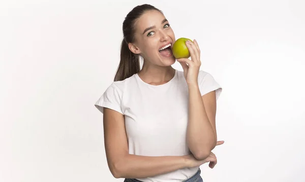 Mujer mordiendo manzana mirando la cámara de pie en el estudio — Foto de Stock