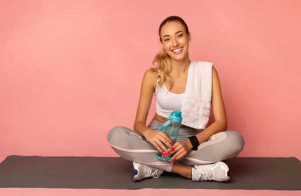 Positief meisje zitten op fitness mat rusten over roze achtergrond — Stockfoto
