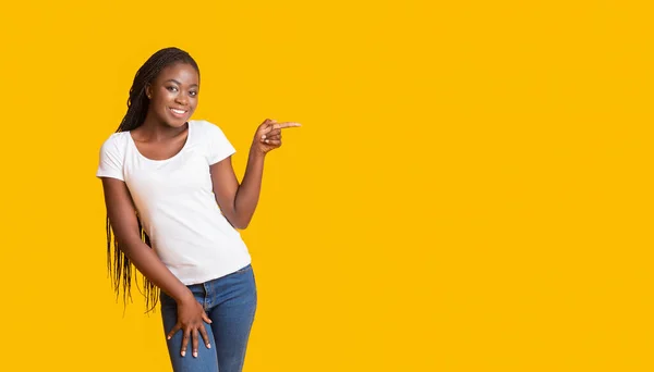 Сексуальная черная девушка, указывающая на пустое пространство на желтом фоне — стоковое фото