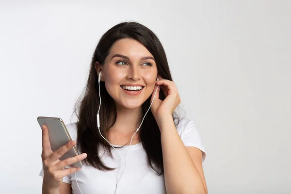 Jovem mulher em fones de ouvido ouvir música no celular, fundo branco — Fotografia de Stock